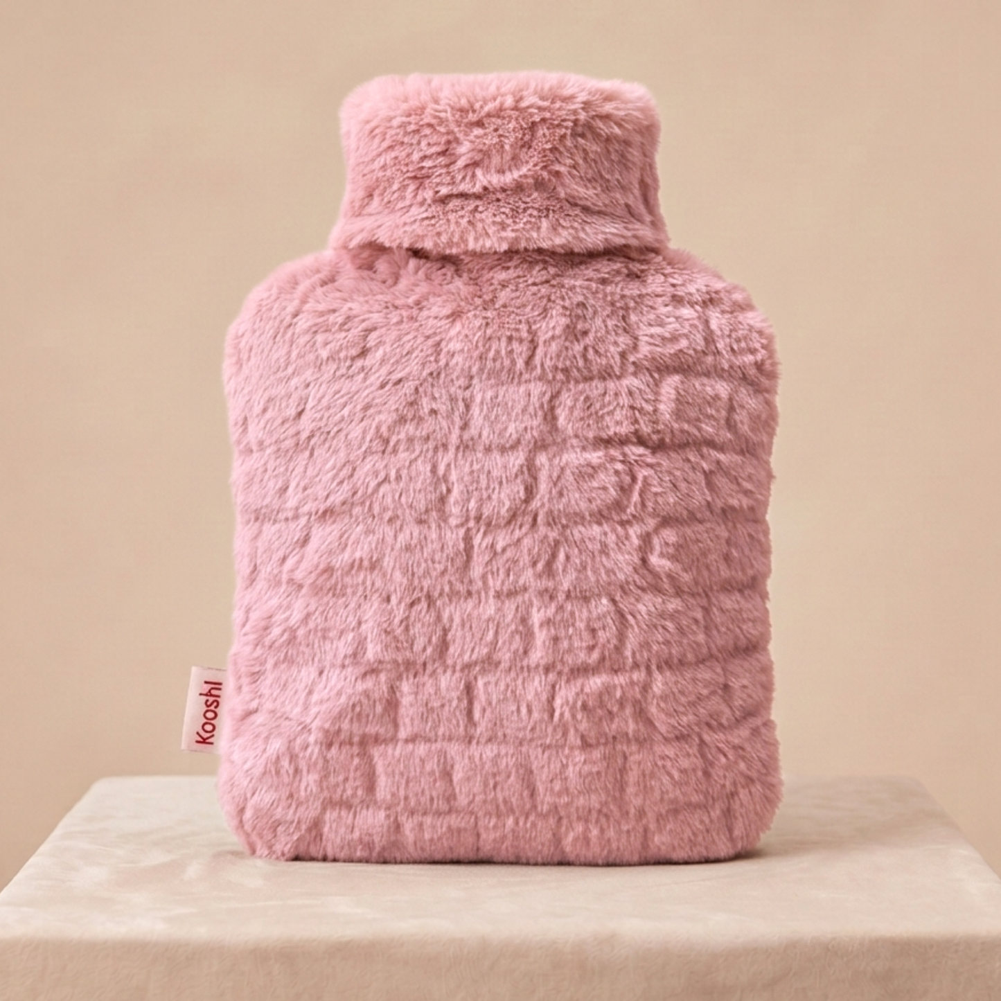 Pink fuzzy hot water bottle on a beige surface with a beige background