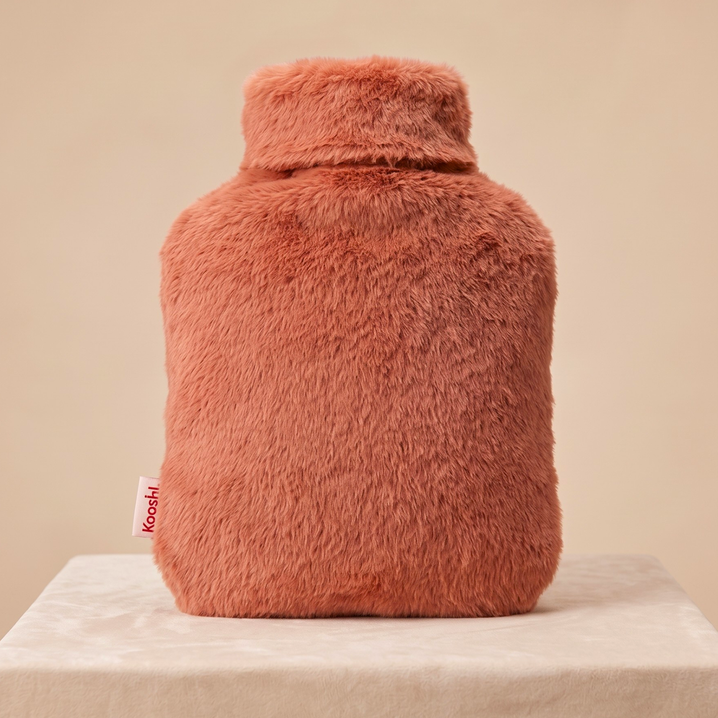 Fluffy pink hot water bottle on a beige background